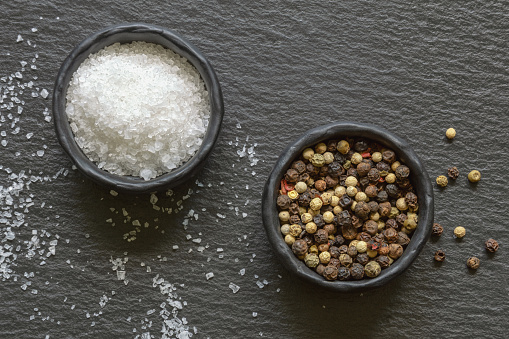 Sea salt and peppercorns in  small  dishes on black background