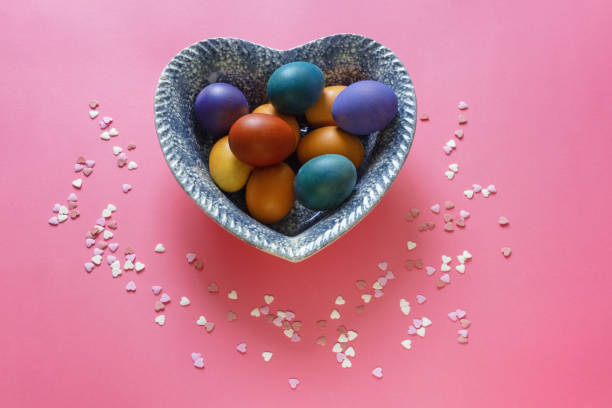 Colorful Easter eggs in heart-shaped plate on pink background