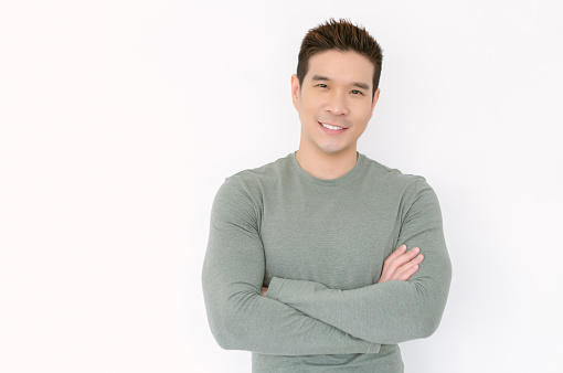 Portrait of happy young Asian handsome man in olive t-shirt standing with crossed arms and looking at camera isolated on white background. Positive emotion, peace of mind, no stress concept.