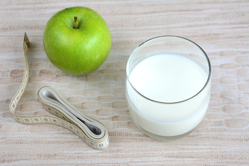 glass of milk, green apple and metre on pastel background