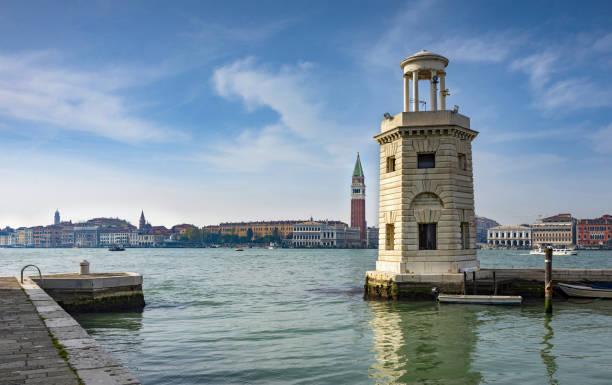 Venice, Italy, April 3, 2016: View of the lighthouse Faro San Giorgio Maggiore in Venetian Lagoon. In the background is the St Mark's Campanile. The entire Venetian Lagoon is listed as UNESCO World Heritage Site.