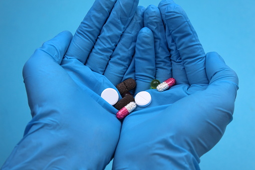 Female hands in medical gloves hold medicines in the form of tablets and capsules in the palm of their hand.
