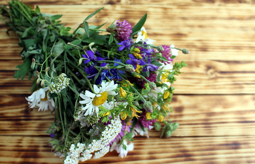 A bouquet of wild flowers lies on a wooden background.