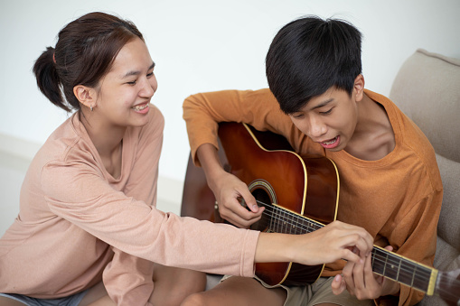 Asian woman teaching Asian man to play guitar