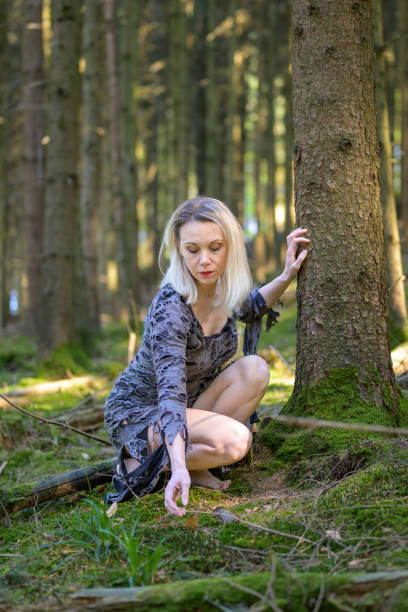 istock Elegant blond woman reaching down to a mossy forest floor 1403634543