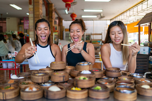 Group of Asian woman tourist eating Chinese food steamed dumpling in bamboo steamer with chopsticks on the table in Chinese restaurant. Happy female friends enjoy eating and travel together on summer vacation.