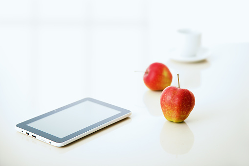 tablet pc with apple and coffee cup with reflections on table