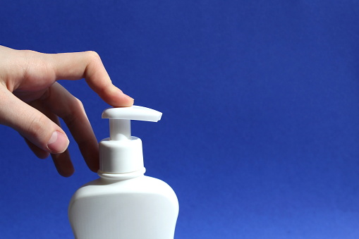 A woman's finger presses on the dispenser of a white vial.
