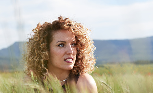 white woman in black dress with gold detail, curly hair, looking at the horizon outdoor