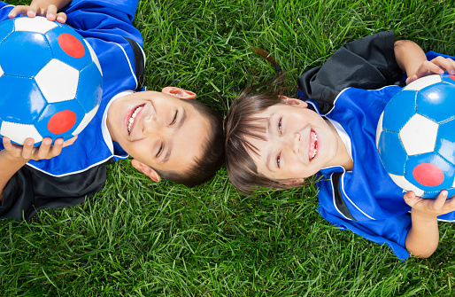Above view of Mixed raced young sibling wearing blue soccer uniform laying on grass.