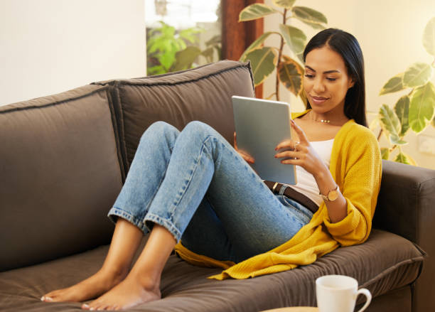 istock Woman using her tablet while comfortable and relaxing in a bright living room. A young female lying on a sofa scrolling on her digital tablet at home using modern technology during lockdown 1403640814
