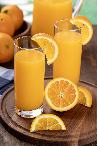 Two glasses of orange juice with sliced oranges on a wooden tray and pitcher in background