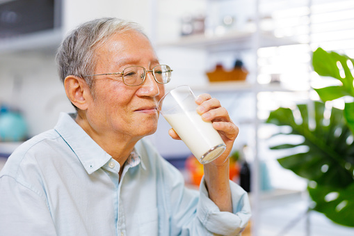 asian senior man drinking a glass of fresh milk at kitchen in the morning