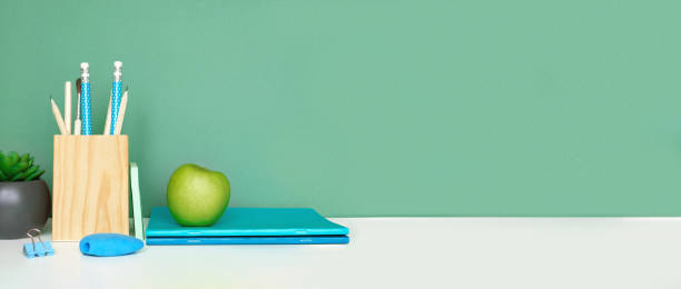School equipment on white table, green wall background. Education backdrop. Wooden school supplies, notepad, pencils and cactus plant. Back to school. Student Desk . Stationery for study. Work at home