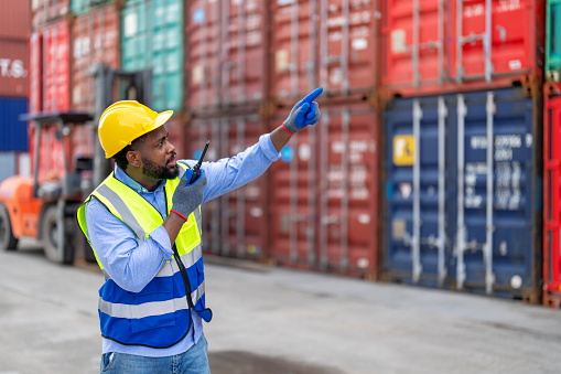African man worker using walkie talkie to communication with colleague at container yard. Container yard warehouse, Cargo Shipping Import and Export industry. Logistic shipping yard business.