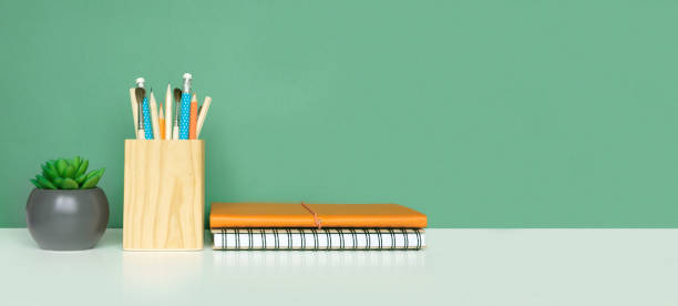 istock School equipment on white table, green wall background. Education backdrop. Wooden school supplies, notepad, pencils and cactus plant. Back to school. Student Desk . Stationery for study. Work at home 1403655790