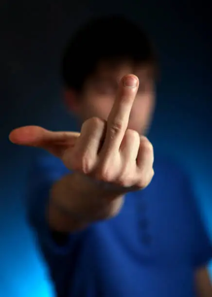 Young Man on the Dark and Blurred Background showing Middle Finger Gesture