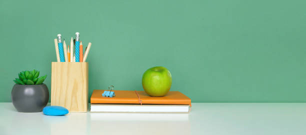 istock School equipment on white table, green wall background. Education backdrop. Wooden school supplies, notepad, pencils and cactus plant. Back to school. Student Desk . Stationery for study. Work at home 1403658220