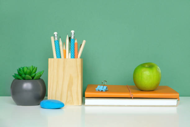 istock School equipment on white table, green wall background. Education backdrop. Wooden school supplies, notepad, pencils and cactus plant. Back to school. Student Desk . Stationery for study. Work at home 1403658275