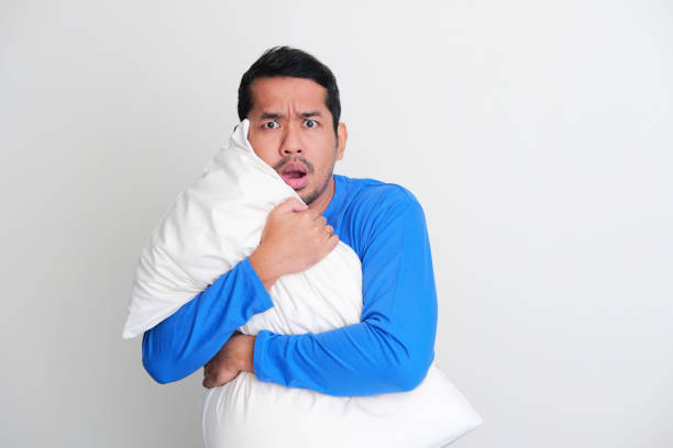 istock Adult Asian man hugging a pillow while showing scared face expression 1403659456