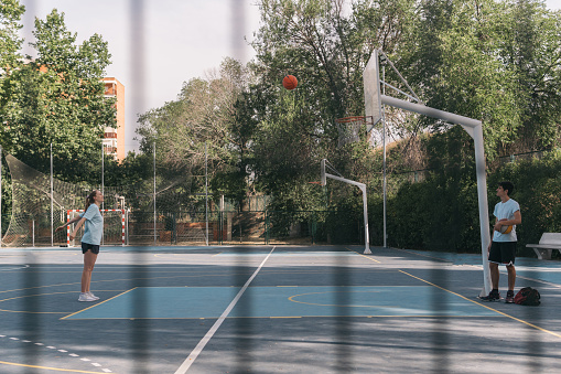 Young girl scoring a two-point basket on a blue court while a boy who is her rival watches her. Friendship and sport concept