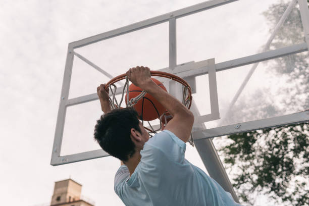 giovane giocatore di basket che fa uno scandaloso slam dunk. - hanging basket foto e immagini stock