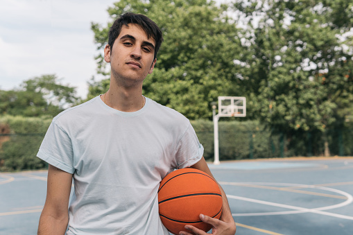 Frontal close-up image of a man in a light-colored t-shirt posing with an orange ball waiting his rival