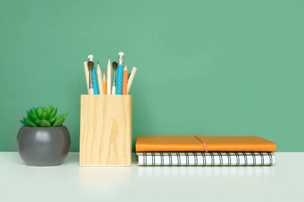 istock School equipment on white table, green wall background. Education backdrop. Wooden school supplies, notepad, pencils and cactus plant. Back to school. Student Desk . Stationery for study. Work at home 1403662749