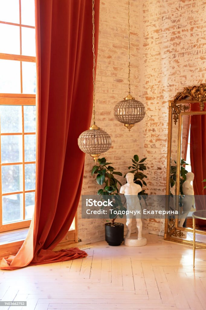 Modern living room in French style. Stylish French interior with big window and curtains, green plant in pot, David sculpture, vintage gold mirror and crystal chandeliers against a brick wall. Bedroom Stock Photo