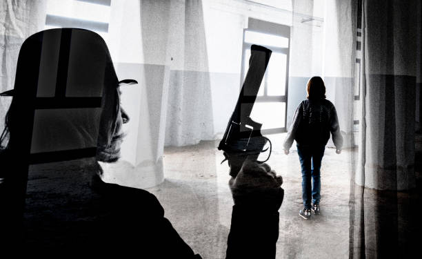 Shot of unrecognizable person with gun superimposed over image of one woman walking in an office corridor.