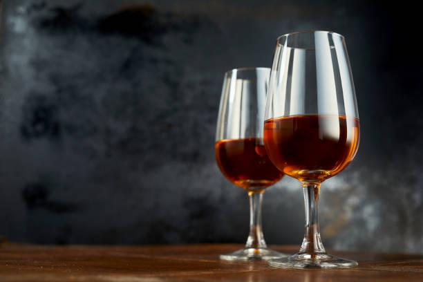 Glasses with sherry wine on table Low angle of shiny wineglasses with sherry drink laced on wooden counter on black background sherry stock pictures, royalty-free photos & images