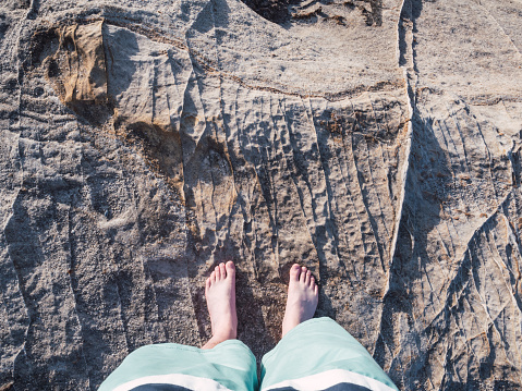 From above bare male feet standing on eroded rock by the sea and with copy space
