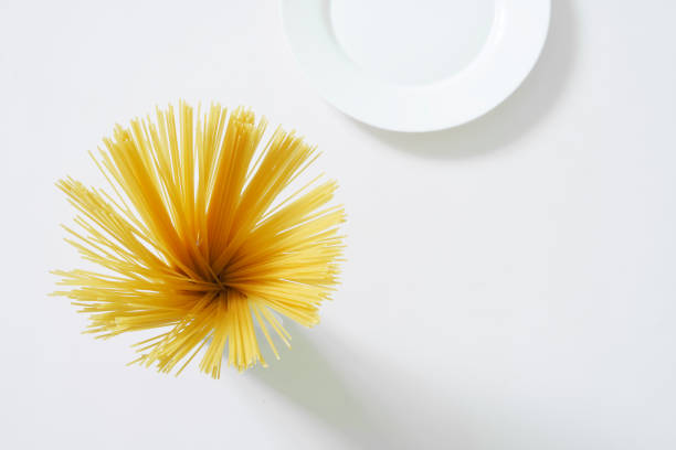 Uncooked Italian durum wheat spaghetti and a clean white plate on a light background. White style. Top view. Free space for an inscription. Daylight