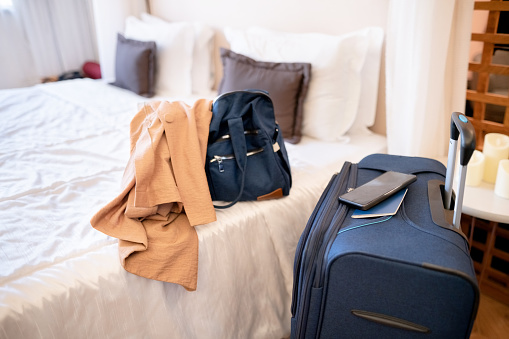 Suitcase in hotel room with jacket and handbag over bed