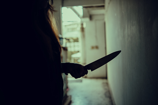 The shadow of a female murderer stood terrifyingly holding a knife and lit from behind.Scary horror or thriller movie mood or nightmare at night Murder or homicide concept.
