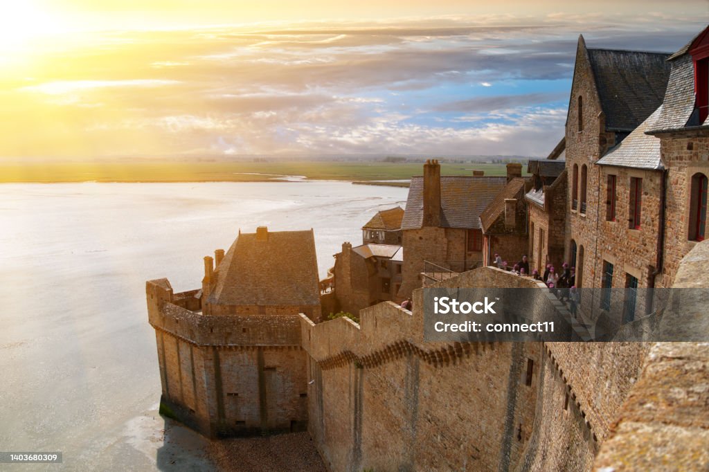 Ancient fortress walls, houses and buildings of the ancient city-fortress of Mont Saint-Michel in the rays of the setting sun Ancient fortress walls, houses and buildings of the ancient city-fortress of Mont Saint-Michel in the rays of the setting sun against the shore of the Atlantic Ocean Mont Saint-Michel Stock Photo