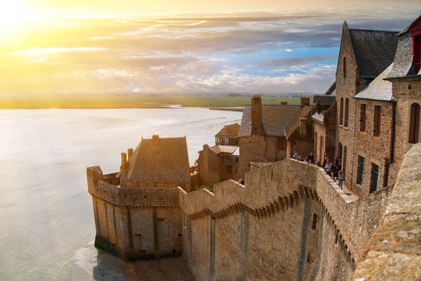 Ancient fortress walls, houses and buildings of the ancient city-fortress of Mont Saint-Michel in the rays of the setting sun Ancient fortress walls, houses and buildings of the ancient city-fortress of Mont Saint-Michel in the rays of the setting sun against the shore of the Atlantic Ocean mont saint michel photos stock pictures, royalty-free photos & images
