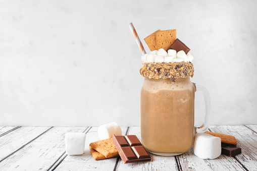 Smores drink in a mason jar glass with ingredients. Side view scene against a white background. Graham crackers, chocolate and marshmallow topping.
