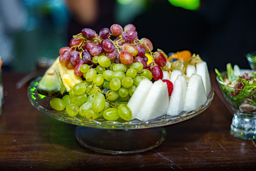 Fruit plate. Stylishly lined fruit: melon slices, grapes. Catering serving on a glass base.