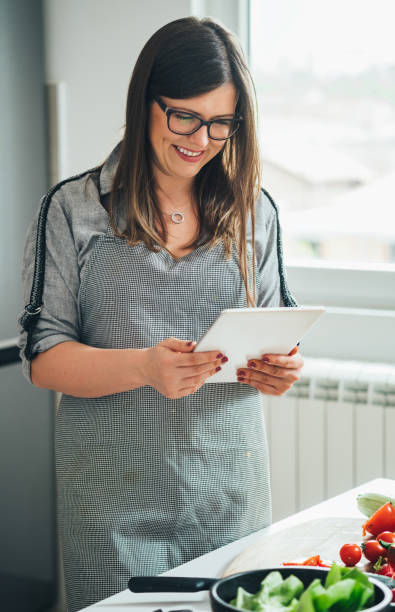 istock Smiling Woman Reading Recipe On A Digital Tablet While Cooking Lunch In The Modern Kitchen 1403689283
