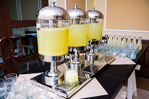 Three beverage dispensers with lemonade standing on the table. Refreshment drinks. Self serving device. Help yourself with drinks. Non-alcoholic beverages.