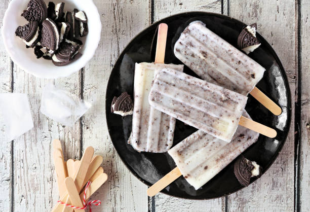 Cookies and cream popsicles on a black plate over white wood