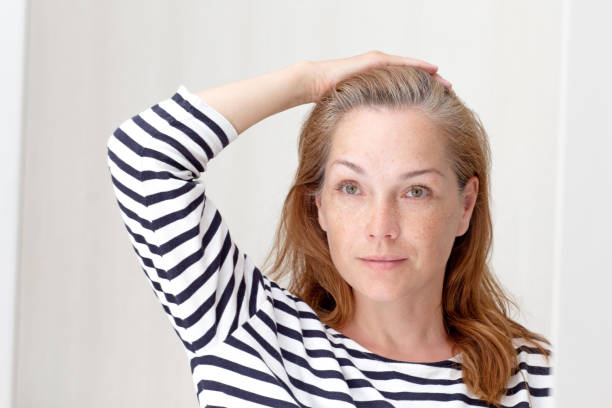istock Smiling woman looking at gray hair in mirror reflection on growth root 1403693772