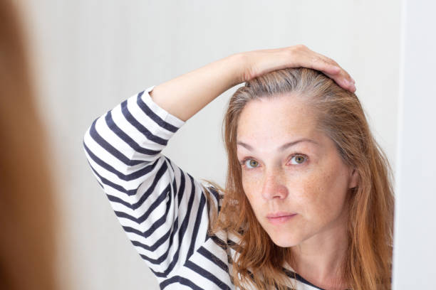 istock Woman looking at gray hair in mirror reflection on growth root 1403693777