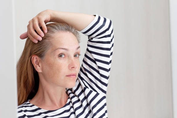 40s woman looking at gray hair in mirror reflection on growth root Beautiful 40s woman looking at gray hair in mirror reflection on growing out root grey hair stock pictures, royalty-free photos & images