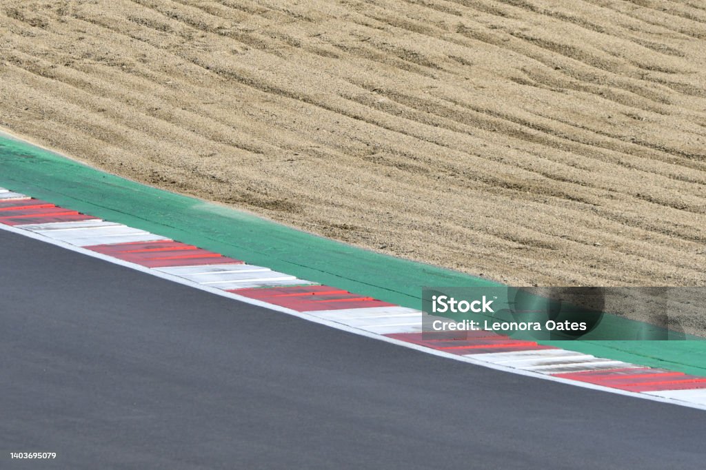 A section of a car race track, with a sandy gravel trap to slow the cars down a red and white chevron marking a corner with green tarmac on the inside and grey tarmac on the outside Silverstone Circuit Stock Photo