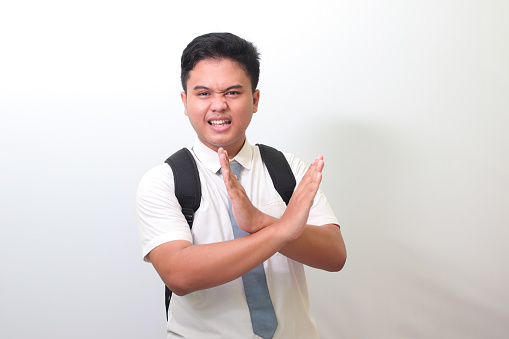 Indonesian senior high school student wearing white shirt uniform with gray tie showing X sign of hands. Teenager refusing an invitation from someone. Isolated image on white background