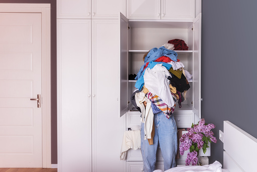 close-up of a young woman holding a large pile of colored crumpled clothes in her hands. The background is the interior of the room, a large white closet. The girl's head is not visible, copy-paste for your design