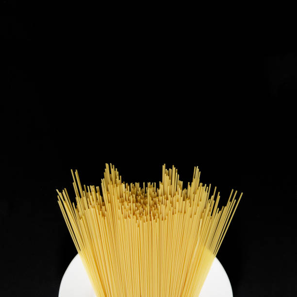 White plate and uncooked Italian durum wheat spaghetti on a black background. View from above. Square. Minimalism. Free space for recording