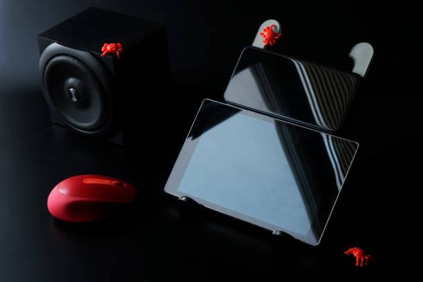 czarny tablet i smartfon na stojaku, głośnik audio, czerwona mysz komputerowa i zabawne pająki- zabawki. czarne tło. minimalistyczna koncepcja nowoczesnych gadżetów i urządzeń. ponure wnętrze technologiczne - toy store zdjęcia i obrazy z banku zdjęć